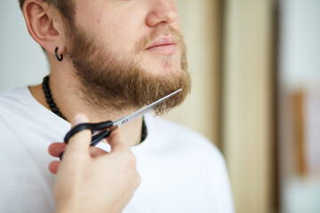 Close-Up of a Young Man Trimming His Beard With Scissors Indoors