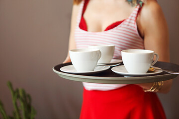 Beautiful young woman wearing bright clothes holding tray with coffee