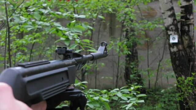 Teenager shoots from a rifle at a target on a tree.