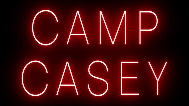 Flickering red retro style neon sign glowing against a black background for CAMP CASEY