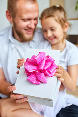 Smiling Father and Daughter Sharing a Gift Box With a Pink Bow Indoors