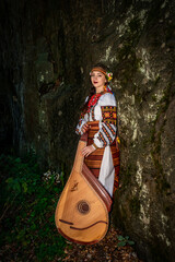 A Ukrainian woman in an embroidered national dress stands near a rock