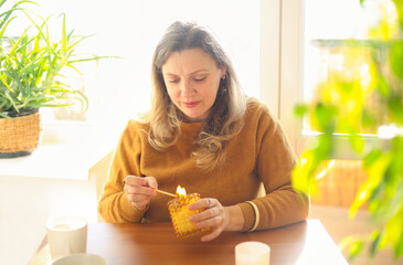 Calm middle-aged woman with lit match lighting candle while sitting at table in cozy room at home