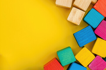 Top view on multicolor toy wooden bricks on yellow background with copy space for text. Children toys on the table.