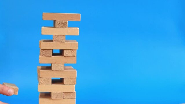 A woman plays wooden game on a blue bright background. The concept of family vacation, holidays, entertainment. A woman's hand takes out a block from a wooden toy tower. Game