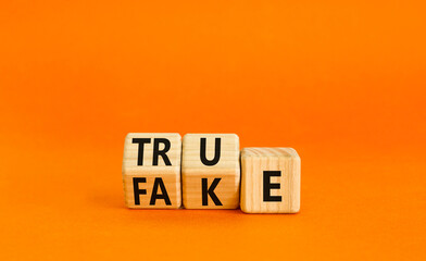 Fake or true symbol. Turned wooden cubes and changed the word fake to true or vice versa. Beautiful orange table, orange background, copy space. Business and fake or true concept.