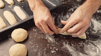Bakery concept. Baker hands kneading dough on table. Making buns. Man forming dough for hot dog buns. Shaping dough. Close-up in 4K, UHD