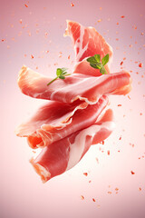 Delicate slices of prosciutto with fresh parsley leaves tumble gently, displayed on a sofy pink background. 

