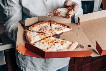 Man Eating Pizza on Kitchen. Pizza in a box, food to go.