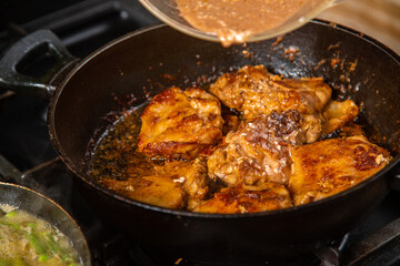 Chicken pieces in spices are fried in a frying pan and sprinkled with soy sauce