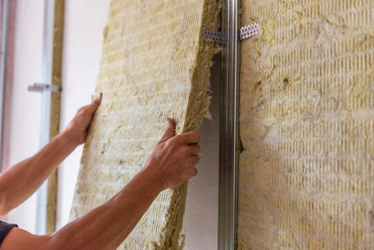 Worker insulating a room wall with mineral rock wool thermal insulation.