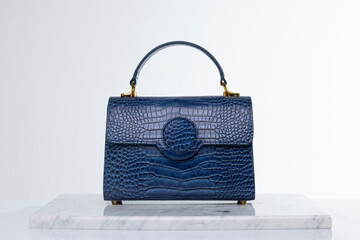 Luxury fashionable navy blue color crocodile skin bag on marble and white background in studio