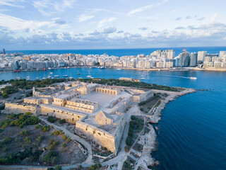 Fort Manoel at sunset with Silema skyline. Higher altitude aerial view on fort and harbor at golden hour. Natural blue and golden colors with clouds in the sky.