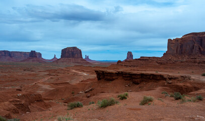 Desert landscape with red rocks and dry vegetation on red sands in Monument Valley, Navajo Nation,  Arizona - Utah