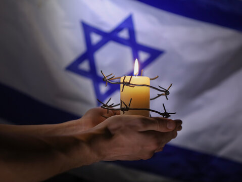 Flag of Israel, barbed wire and burning candle on black background. Holocaust memory day