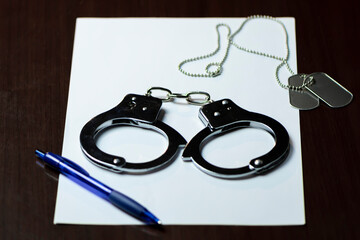 Handcuffs and an army badge on white paper, with a blue pen lying nearby.