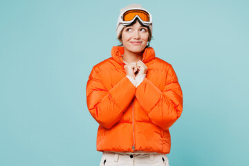 Skier young minded woman she wearing warm padded windbreaker jacket hat ski goggles mask look aside making wish travel rest spend weekend winter season in mountains isolated on plain blue background. © ViDi Studio