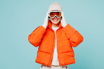 Young smiling happy woman wear warm padded windbreaker jacket hat ski put hands on goggles mask...