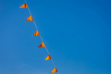 Selective focus of pennant orange flags waving in the air with blue clear sky as background, Orange colour fever is a phenomenon in the Netherlands that occurs during major events in Dutch culture.
