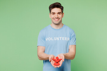 Young fun man wear blue t-shirt white title volunteer hold in hands palms little paper angel...