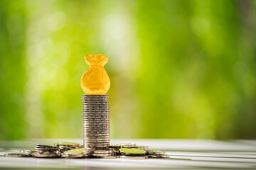 Stack coin and money bag as destinations of success put on the top  put on the wood on sunlight in the public park, Loan or saving money for future investment concept.