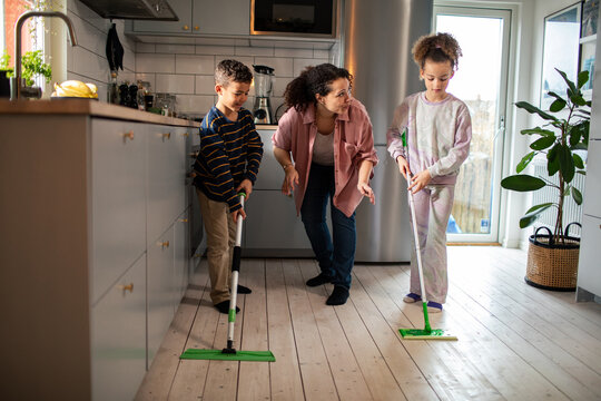 Mother and children sweeping the kitchen floors at home