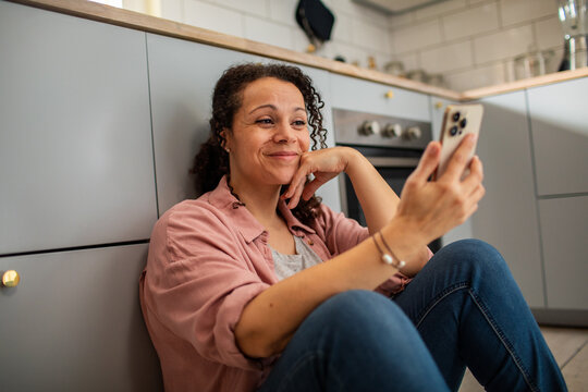 Smiling young woman using smartphone on kitchen floor