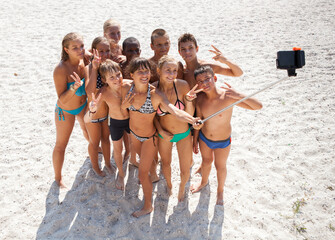 A cheerful group of children on a sandy beach taking a selfie - 714839541