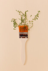 Paint brush with white handle and plant with green small leaves on beige studio background