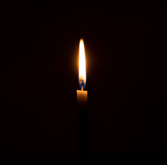 A single burning candle flame or light glowing on an orange candle on black or dark background on table in church for Christmas, funeral or memorial service with copy spac