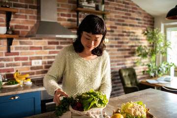 Japanese woman unpacking bought vegetables in home kitchen