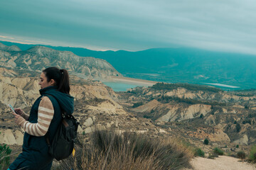 Fototapeta premium Connecting in Digital Nature: In this amazing corner of the badlands, a young woman immerses herself in the lunar beauty while checking her phone. Shocked by the spectacle of gullies, canyons and ravi