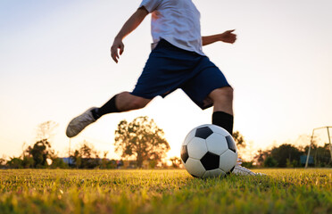 Soccer player kicking ball. Action sport outdoors playing football for exercise at green grass field under the twilight sunset.