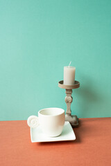 White coffee cup with candle on red table. mint green wall background