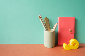 Pink diary notebook and writing supplies stationery in holder on red desk. mint green wall background