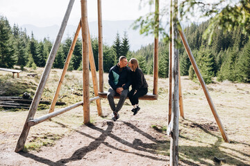 a man and a woman are traveling in the mountains. a couple sits on a large wooden swing high in the mountains. autumn in the mountains
