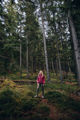 Obraz premium a woman in a pink jacket travels through the mountains. go on a hike with friends. a woman stands in the middle of a spruce forest