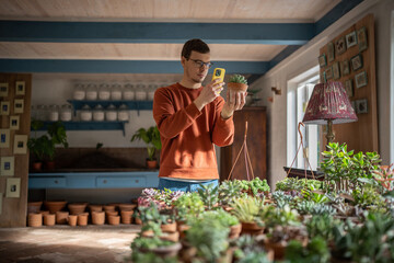 Man plant seller takes photos of potted plants on smartphone to sell online. Plant lover...