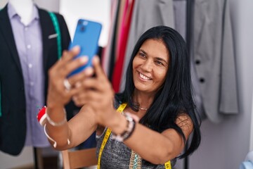 Middle age hispanic woman tailor make selfie by smartphone at tailor shop