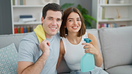 Beautiful couple sitting on sofa hugging each other holding products to clean at home