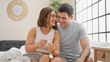 Beautiful couple holding pregnancy test smiling at bedroom