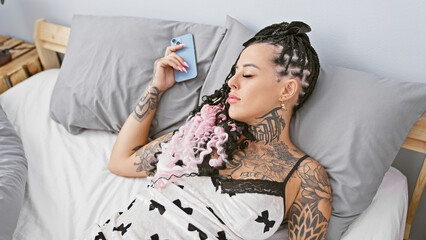 Attractive young hispanic woman deeply sleeping, holding smartphone in her cozy bedroom,...