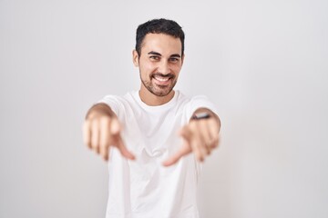 Handsome hispanic man standing over white background pointing to you and the camera with fingers, smiling positive and cheerful