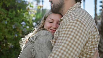 Fototapeta premium A content woman embraces a man outdoors, surrounded by nature and sunlight.