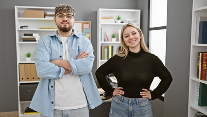 A confident man and woman pose as professional coworkers in a modern office interior, expressing...