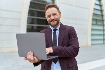 Fototapeta premium Middle age man business worker smiling confident using laptop at street