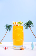 Glass of 100% Orange juice with orange slices fruits on sea beach with white sand. Summer sea vacation and travel concept. Exotic summer drinks.