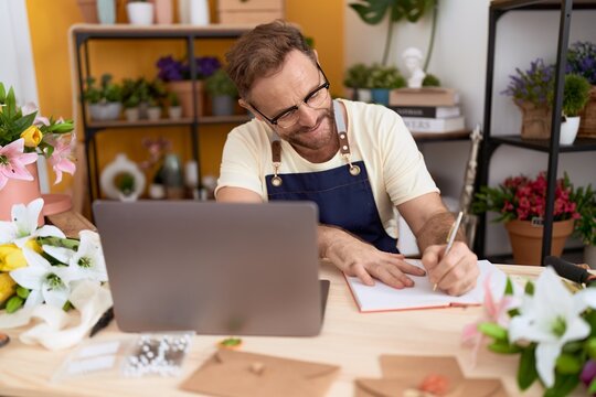 Middle age man florist using laptop writing on notebook at flower shop - Powered by Adobe