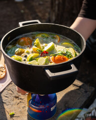 Steaming mulled wine in a black pot with vibrant citrus and apples, cooked on a portable stove in a sunlit outdoor setting