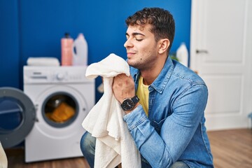 Young hispanic man smelling towel standing at laundry room